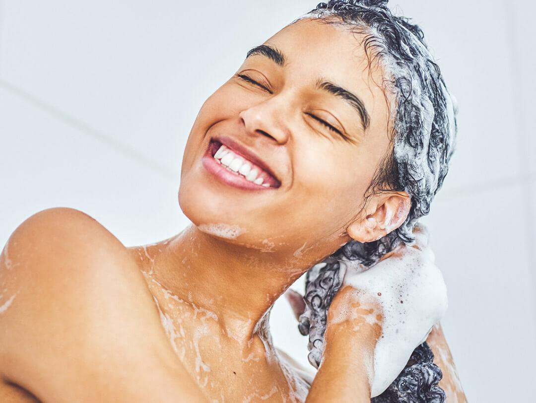 Close-up of a smiling, young woman washing her hair inside the bathroom Desktop