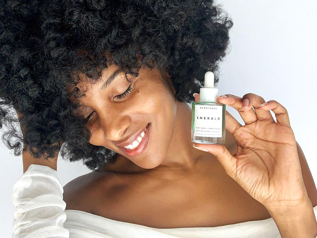 Close-up of a Black woman holding the HERBIVORE Emerald Deep Moisture Glow Oil Desktop