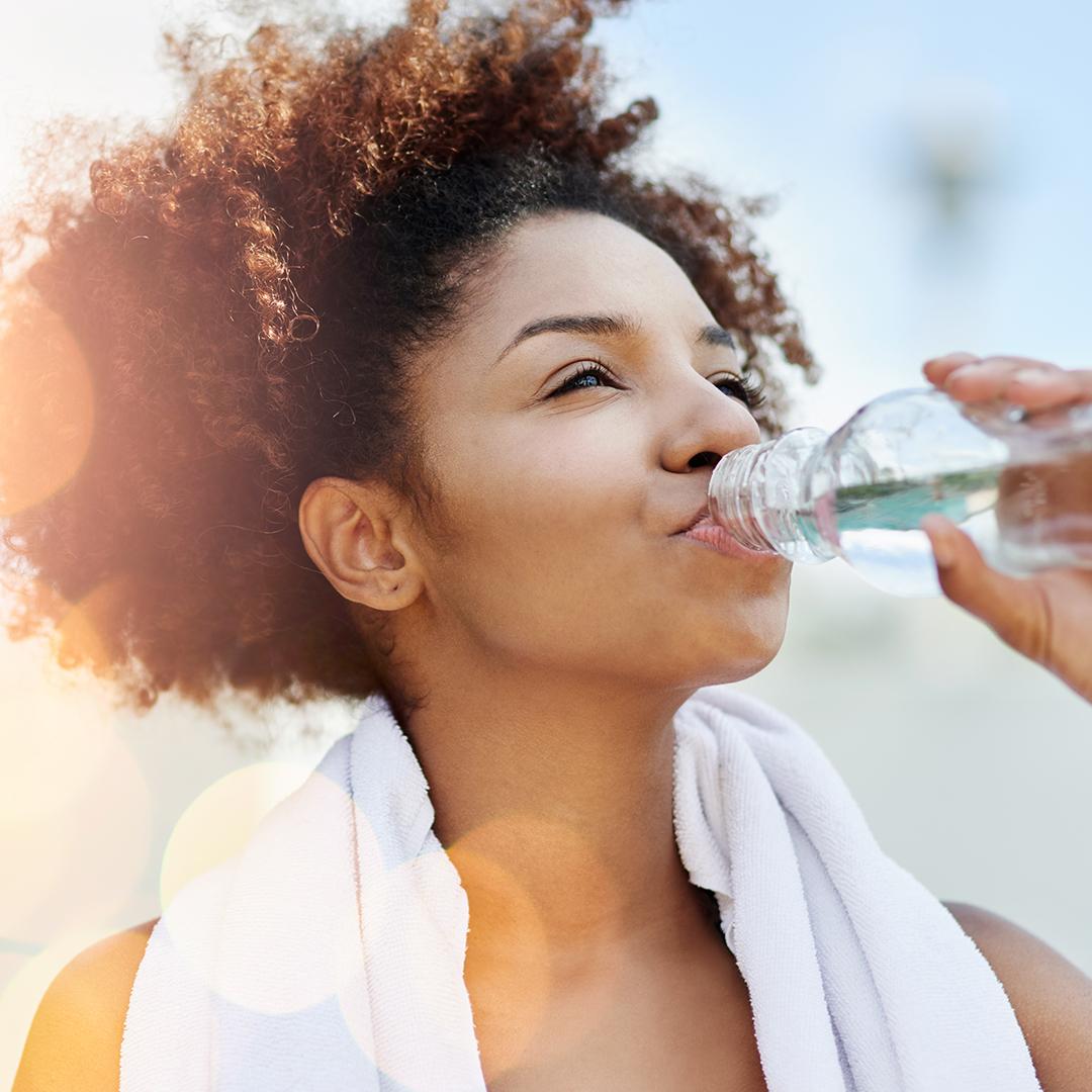 A photo of a woman with a white towel on her neck drinking from a bottle of water Mobile