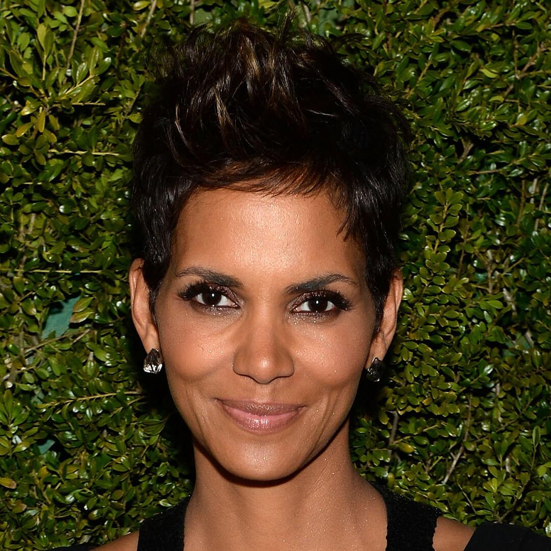Close-up image of Halle Berry rocking a pixie cut hairstyle against a hedge background Mobile