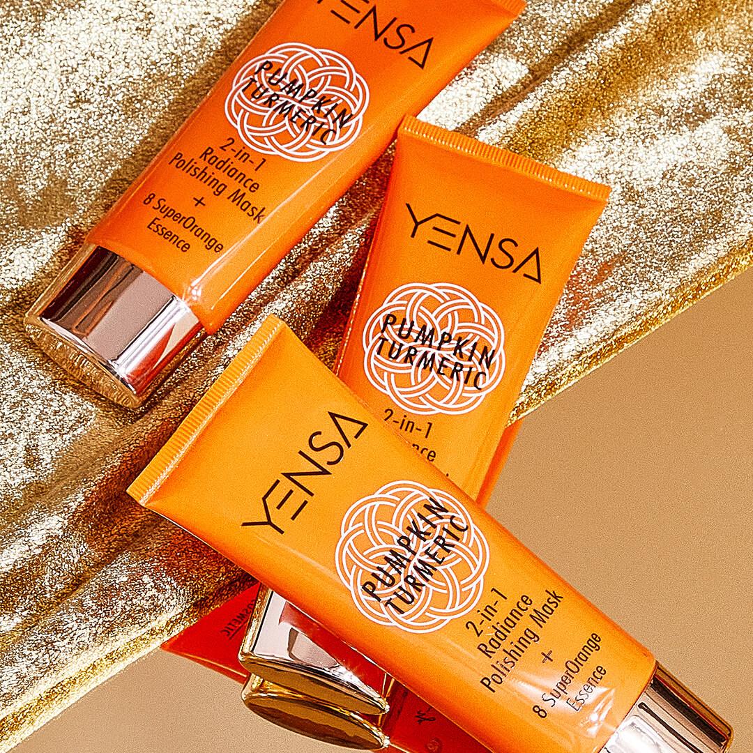 Three tubes of YENSA BEAUTY Pumpkin Turmeric 2-in-1 Polishing Mask on sparkly and shimmery gold cloth Desktop