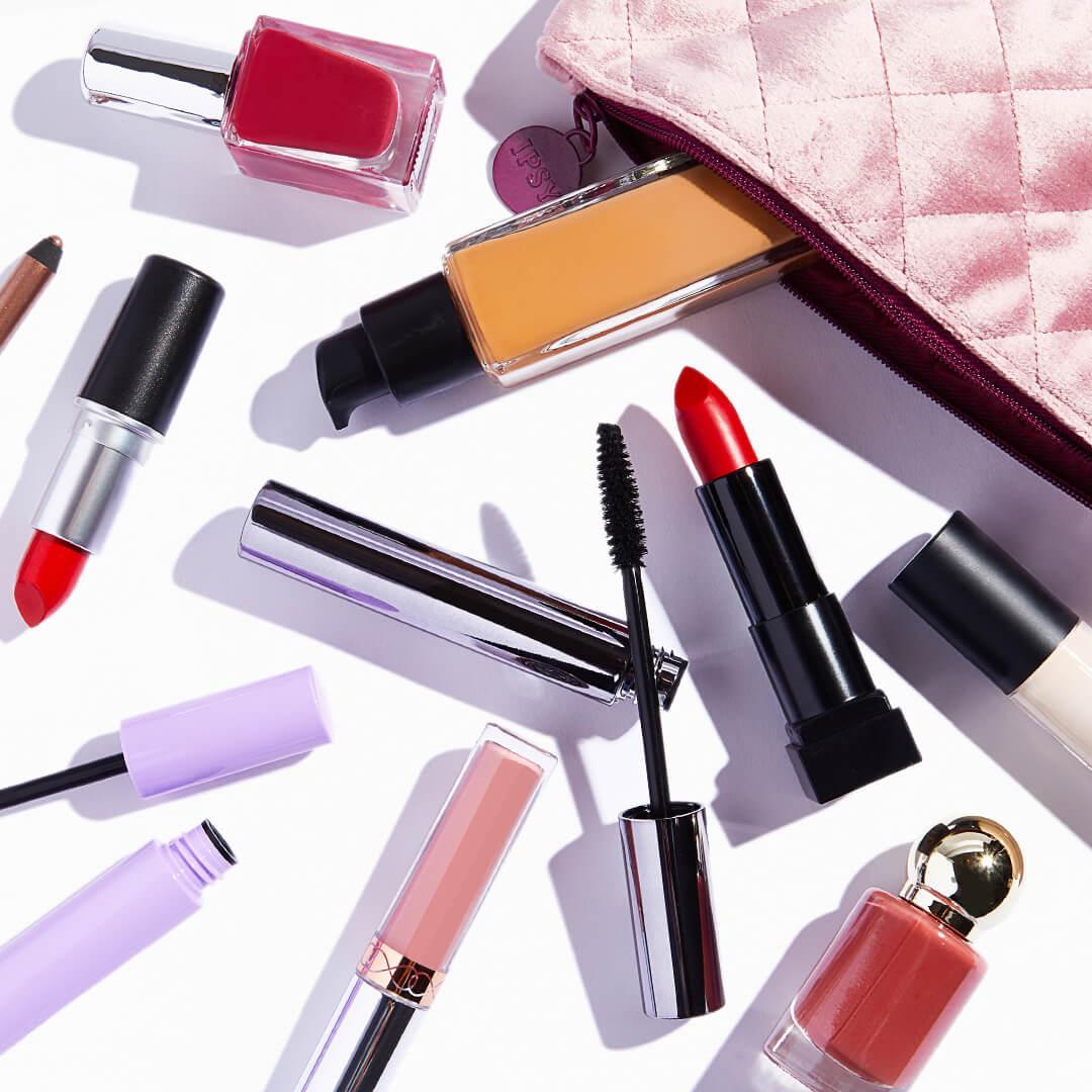 Makeup products, nail polishes, and pink quilted pouch scattered on white background Desktop