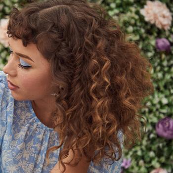 A close-up image of a curly-haired model with partly hidden braids Mobile
