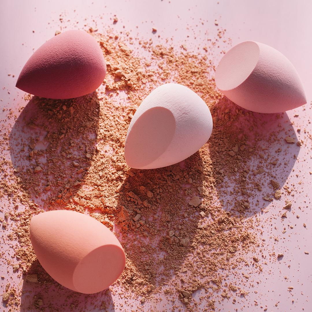 An image of sponges with various colors and cosmetic powder laid on a pink paper Mobile