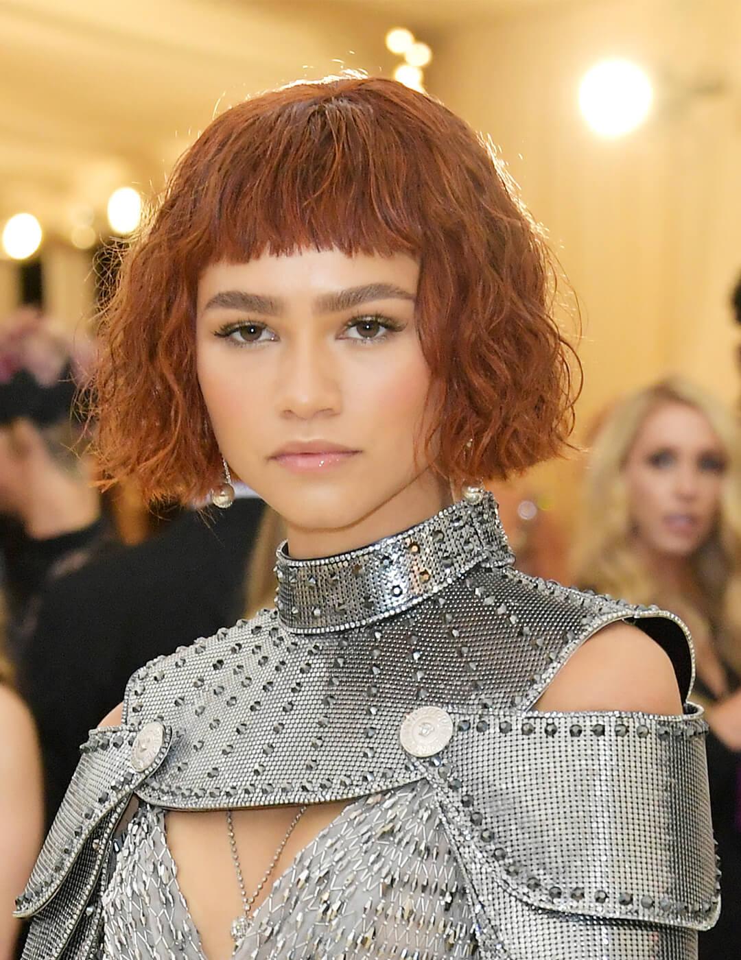 A photo of Zendaya with a Joan of Arc inspired look with super deep copper textured crop hair and a custom Versace dress Desktop