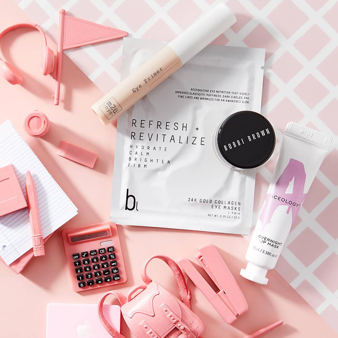 Skincare products from September 2021 IPSY Glam Bag, miniature pink headphones, flag, notebooks, calculator, backpack, and stapler on pink and white tile background Desktop