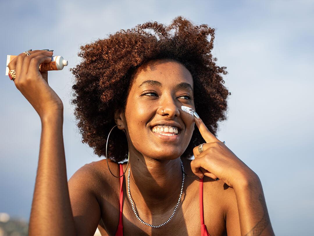 Woman with natural curly hair applies sunscreen to her face Desktop