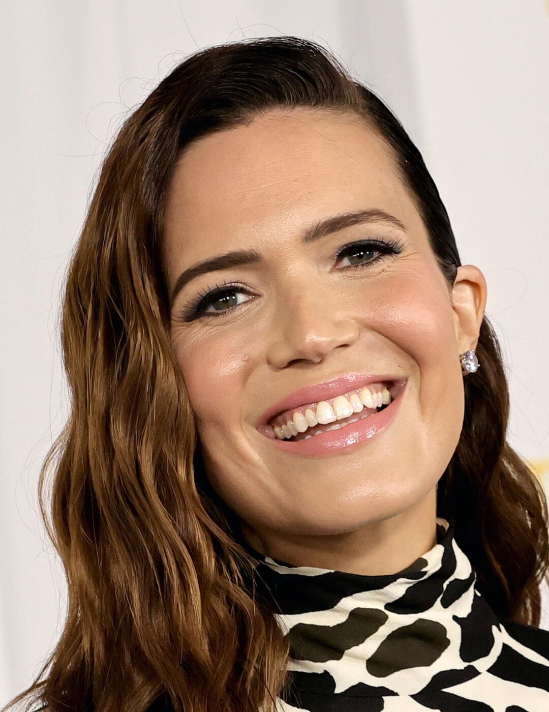 Close-up of Mandy Moore smiling at the camera rocking light pink gloss wearing a printed black and white dress complemented by her diamond earrings Desktop