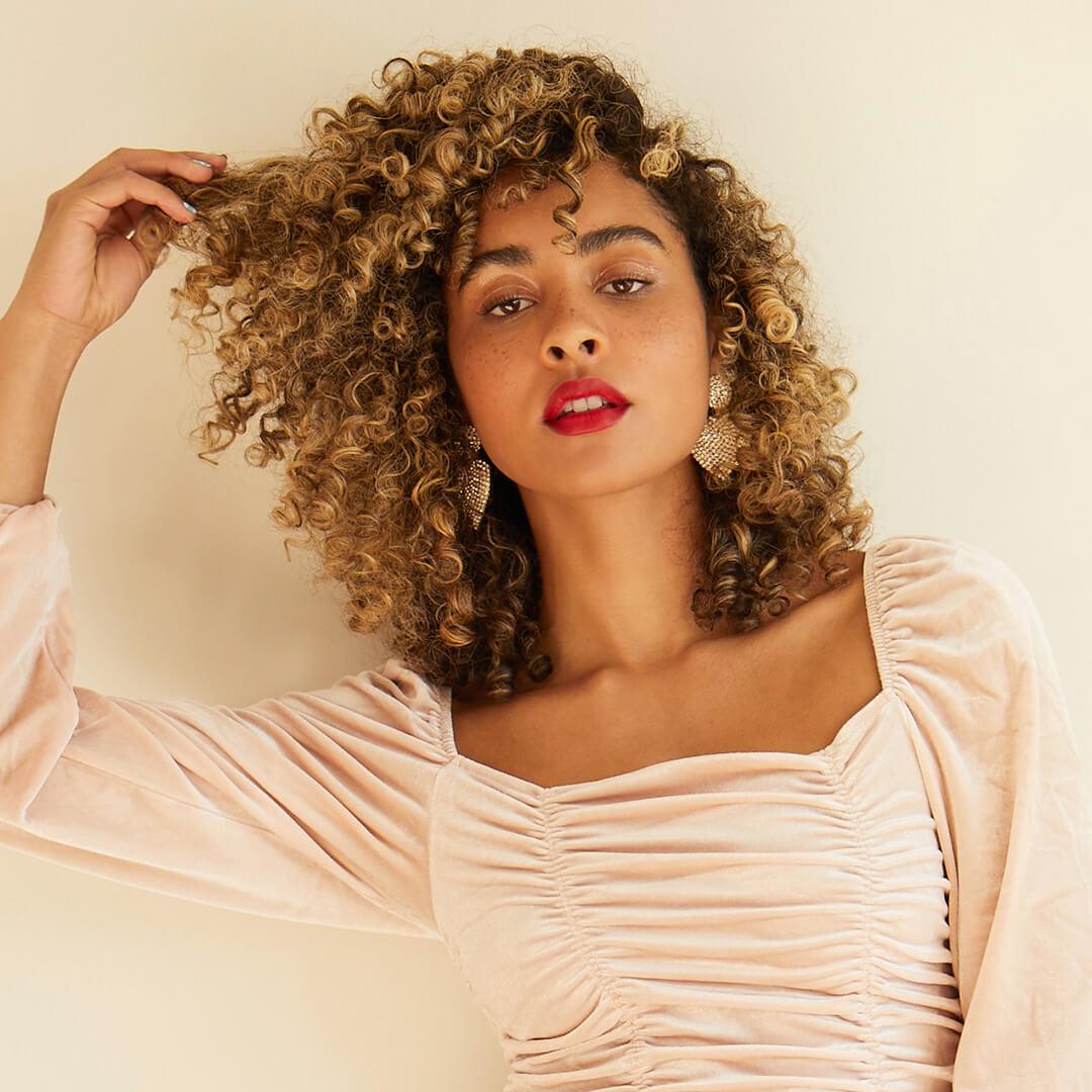 Image of a curly-haired model posing and touching her hair Mobile