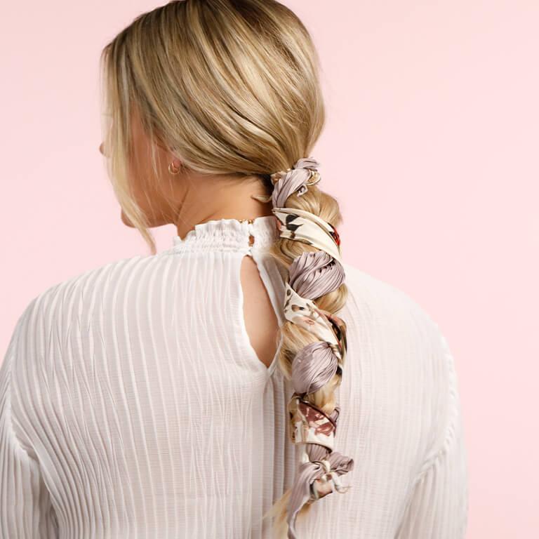 An image of a blonde model showing her braids interlaced with a white and lilac floral scarf Desktop