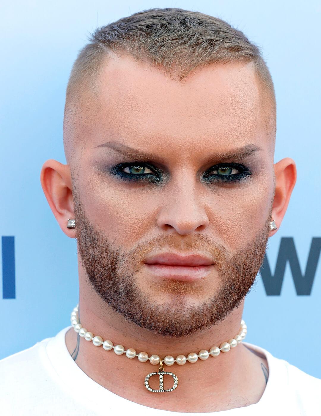August Getty looing fierce in a blue eyeshadow makeup look, white shirt, and pearl choker Mobile