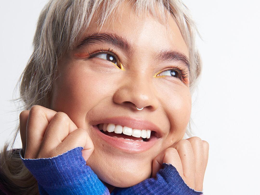 Close-up portrait of a young woman with glowy skin and smiling with hands on face Desktop