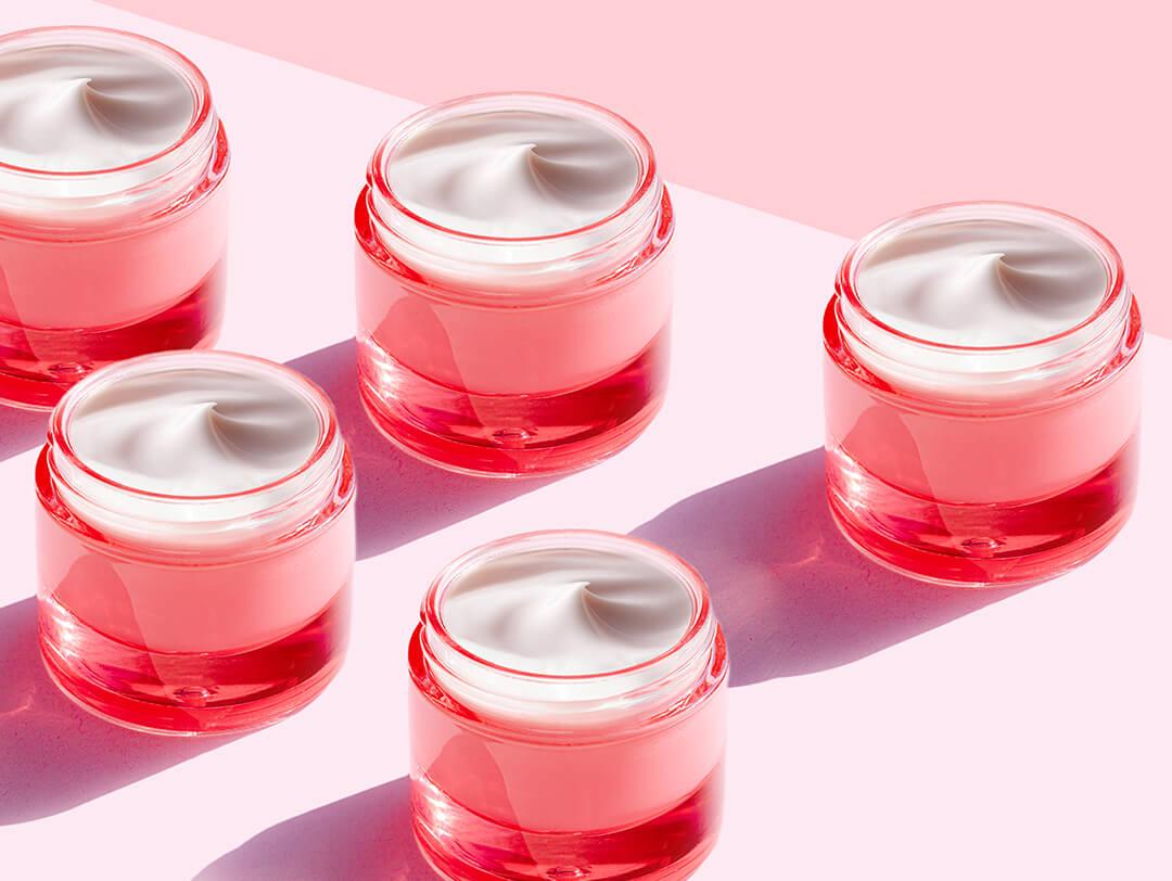 Pink jars of face cream on light pink background Desktop