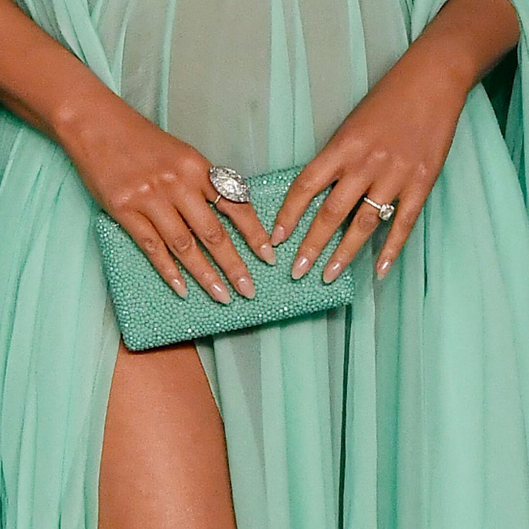 Close-up of Chrissy Teigen's hands with nude nail polish holding a mint green bejewelled purse against her sheer mint green dress Desktop