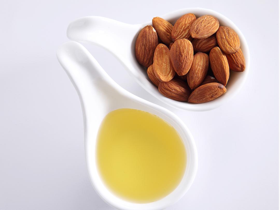A close-up view of a spoonful of almonds and oil in a white spoon with white background Desktop