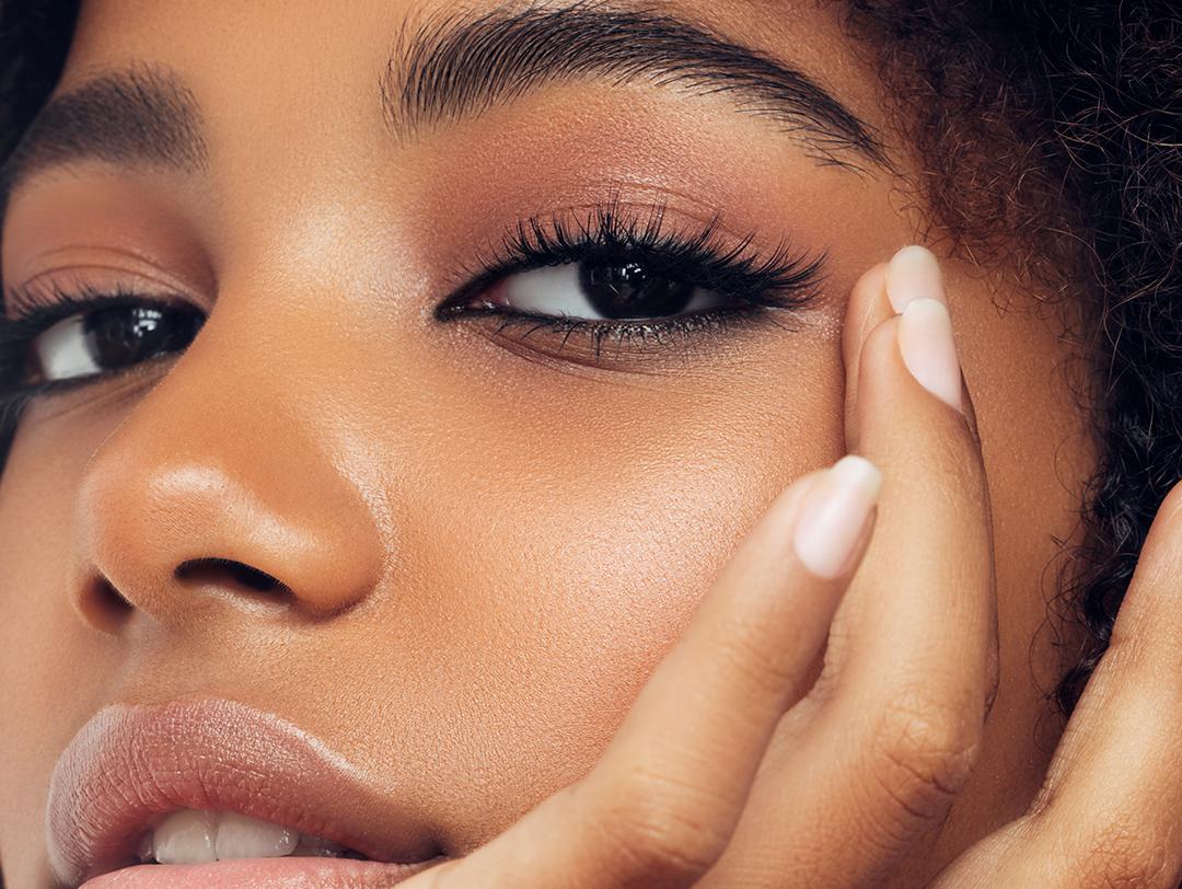 An image of a Black woman wearing a glamorous eyelash extension while touching her face Desktop
