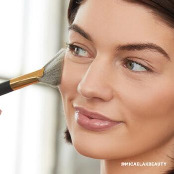 A model using a fan brush in applying highlighter on top of her cheekbone Mobile