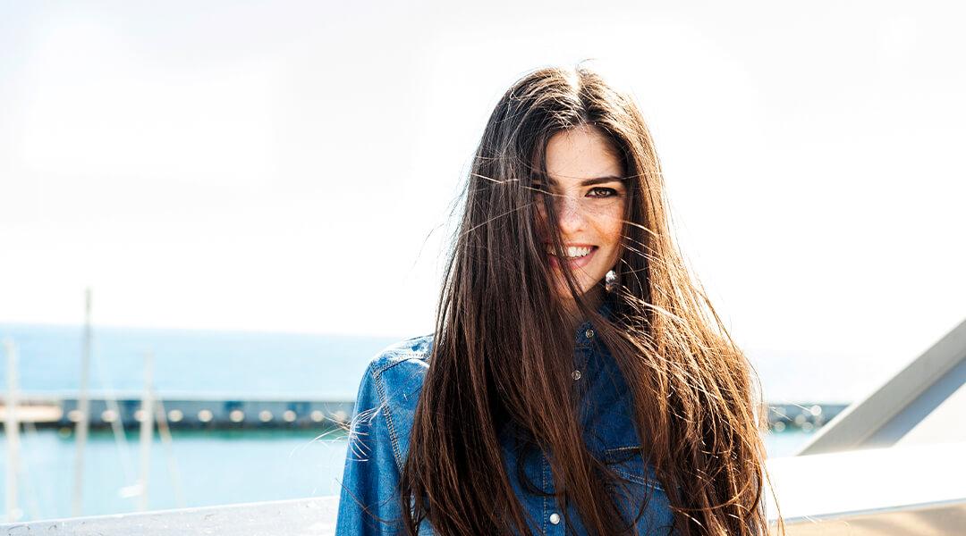 Woman with long hair wearing denim and smiling with harbor view as background Desktop