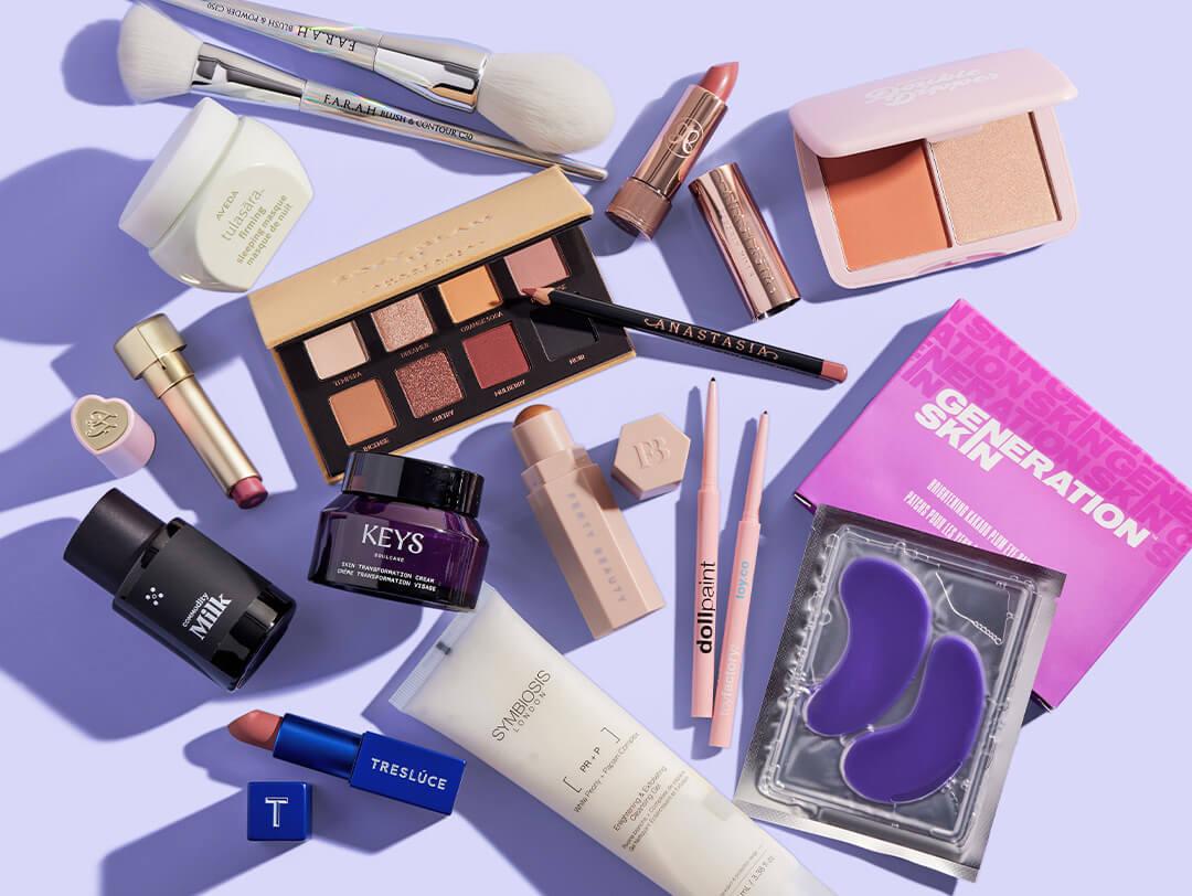 Skincare, makeup, and hair products and tools from various brands scattered on light purple background Desktop