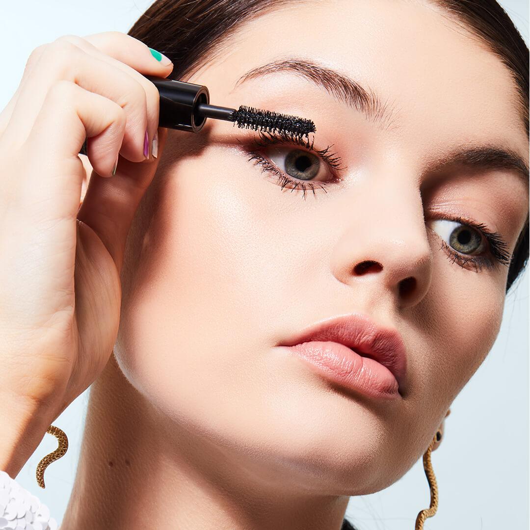 Close-up of a model looking down while applying mascara Mobile