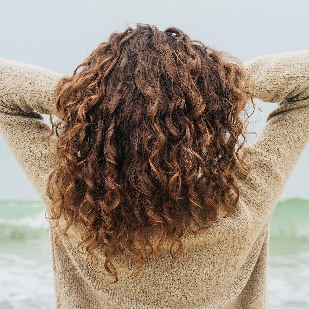 A photo of a woman showing her defined curly hair on a beach background Mobile