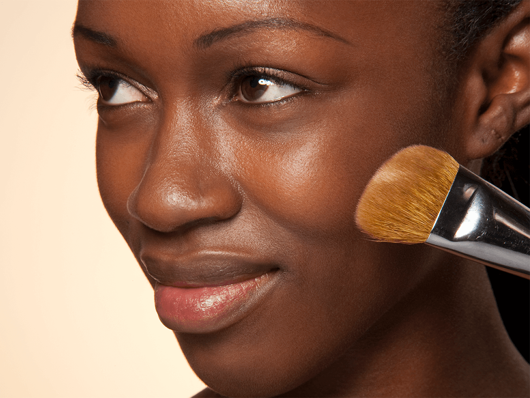 Close-up image of a Black woman putting on face makeup using a makeup brush Desktop