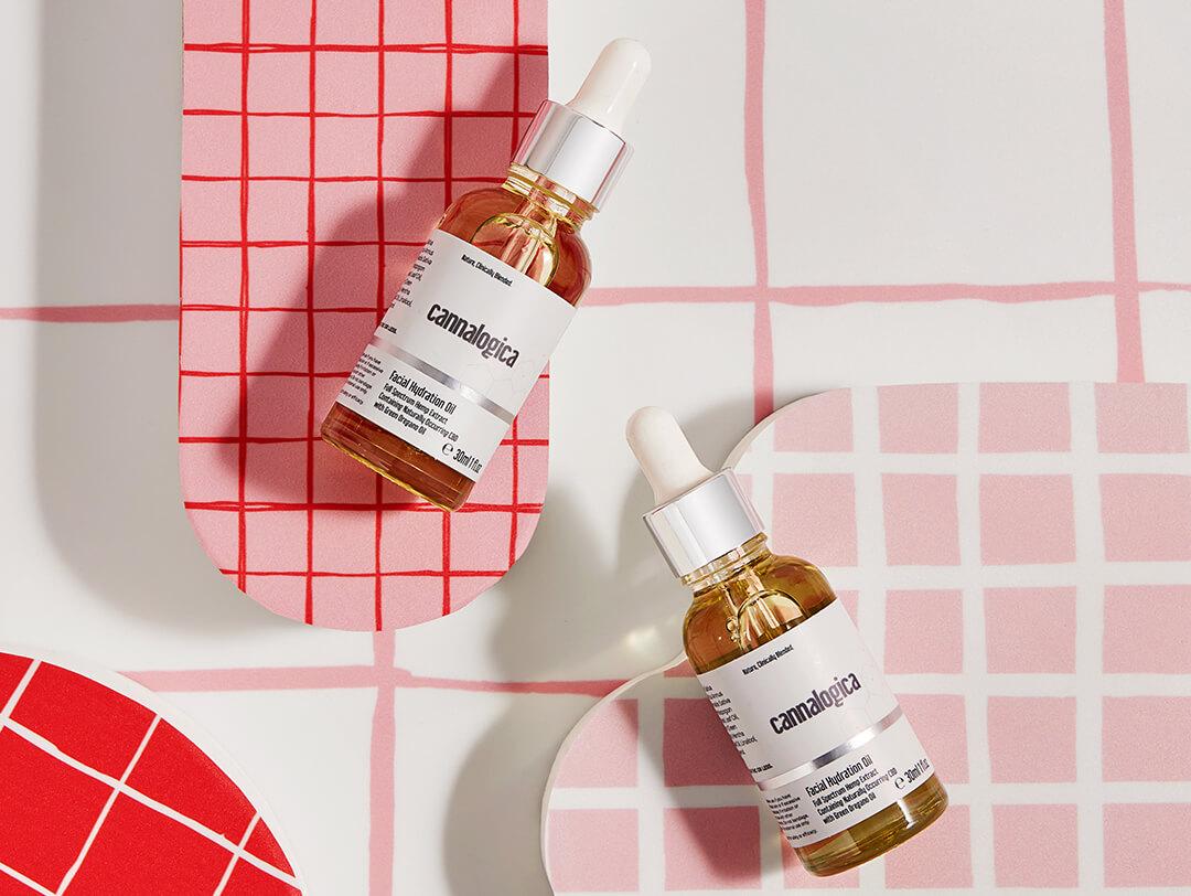 Flat-lay image of two bottles of CANNALOGICA Facial Hydration Oil on white and pink tile background Desktop