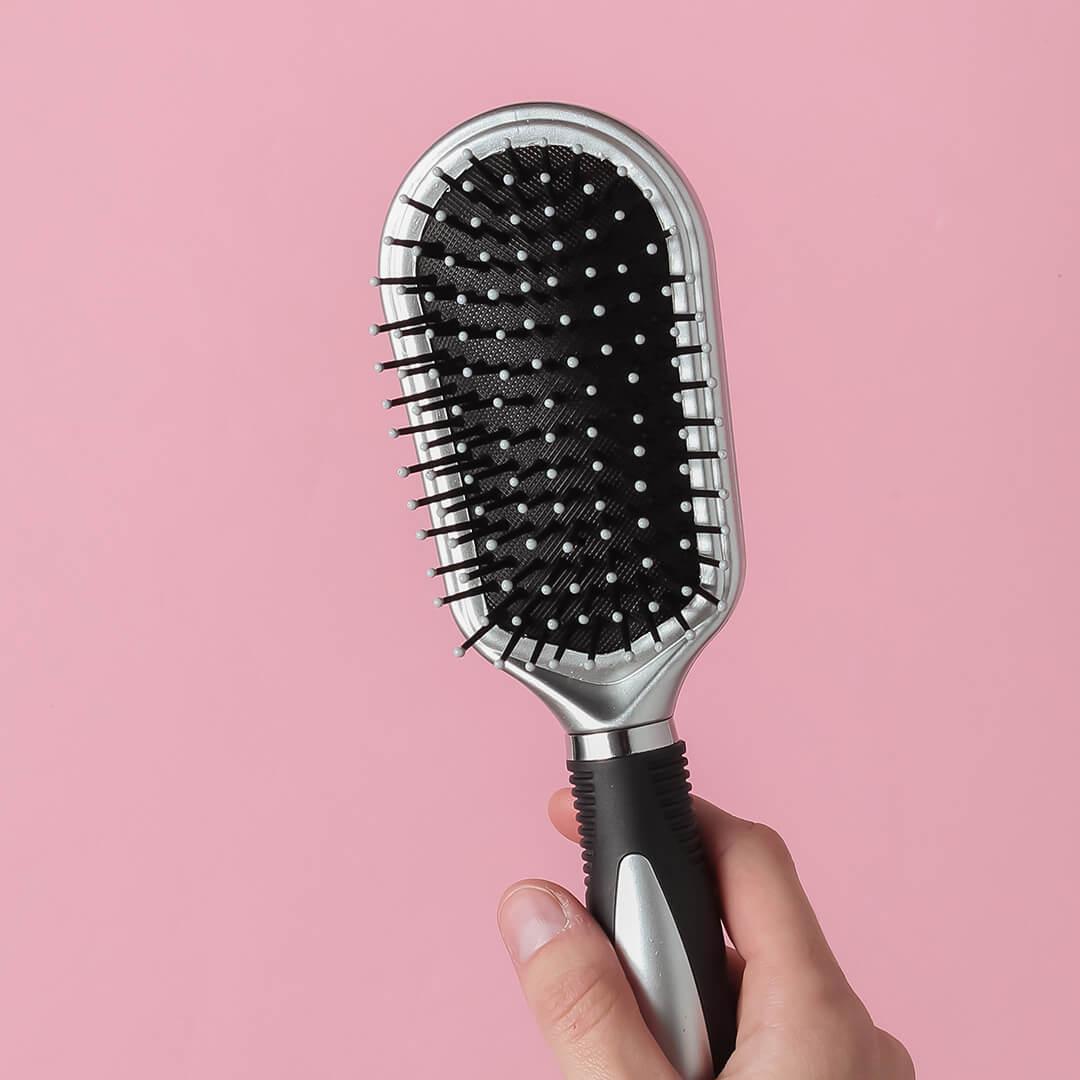 A photo of a mode's hand holding a comb on a pink pastel background Mobile