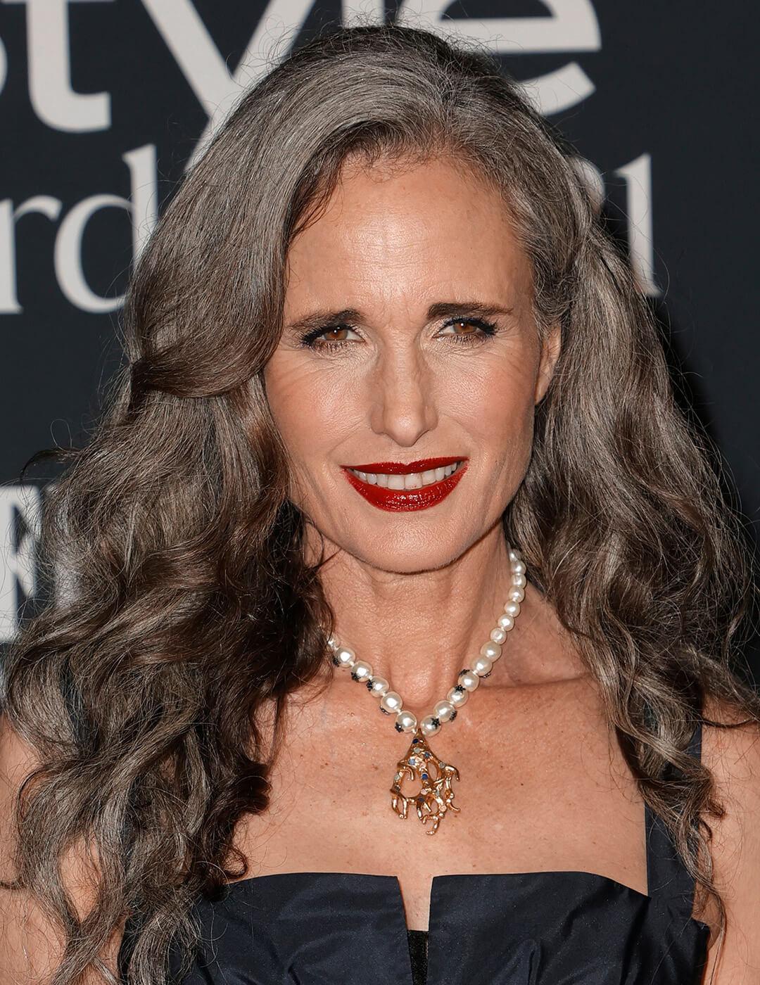 A photo of Andie MacDowell with a smokey eye makeup and red lip look wearing a black dress and a pearl necklace Desktop