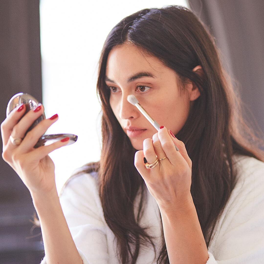 Beautiful young model contouring her nose using a COMPLEX CULTURE makeup brush and holding a compact mirror Desktop