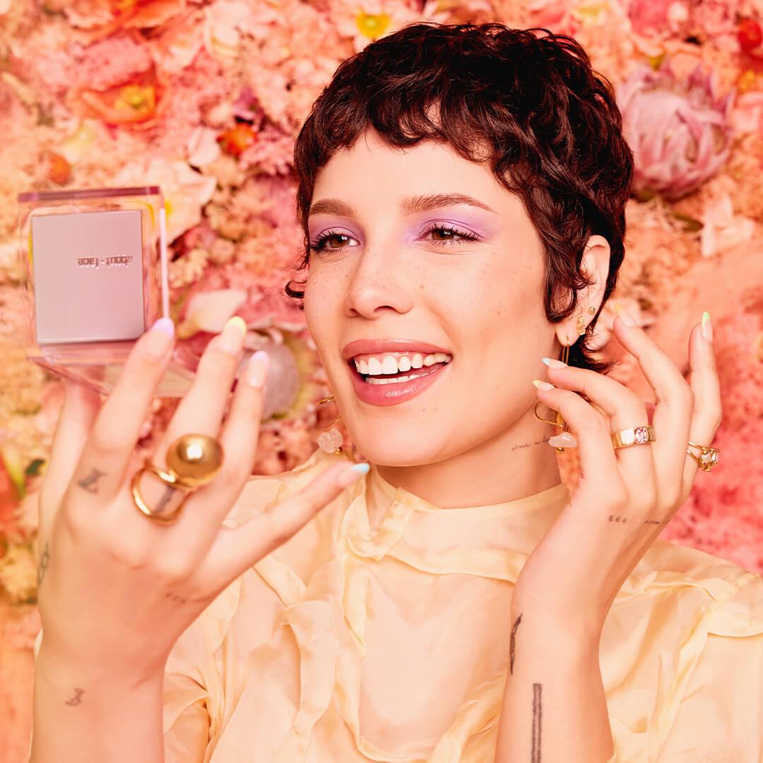 Close-up of a smiling Halsey looking at herself in a compact mirror against floral background Mobile