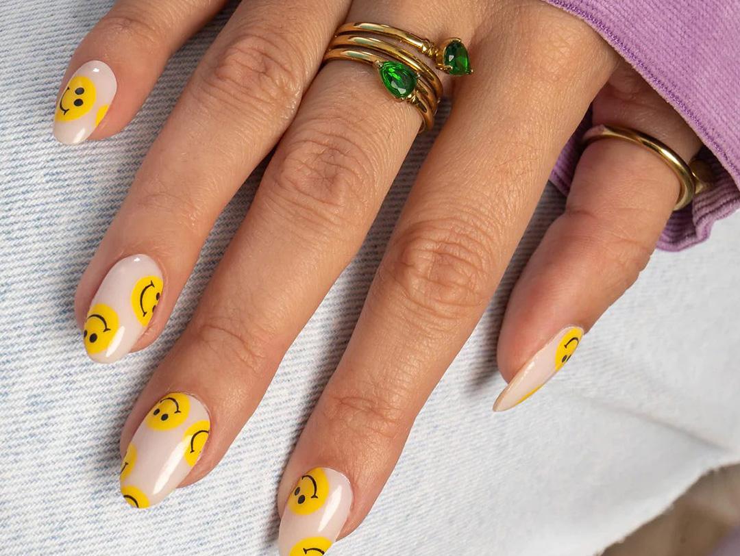 An image of a hand showing a trendy manicure with yellow-smiling face on it lying on a white cloth Desktop