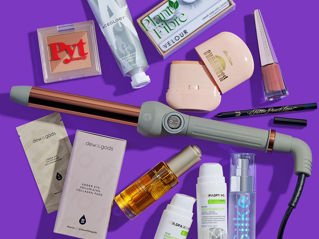 Makeup, skincare, and beauty products and tools from various brands scattered on dark purple background Desktop