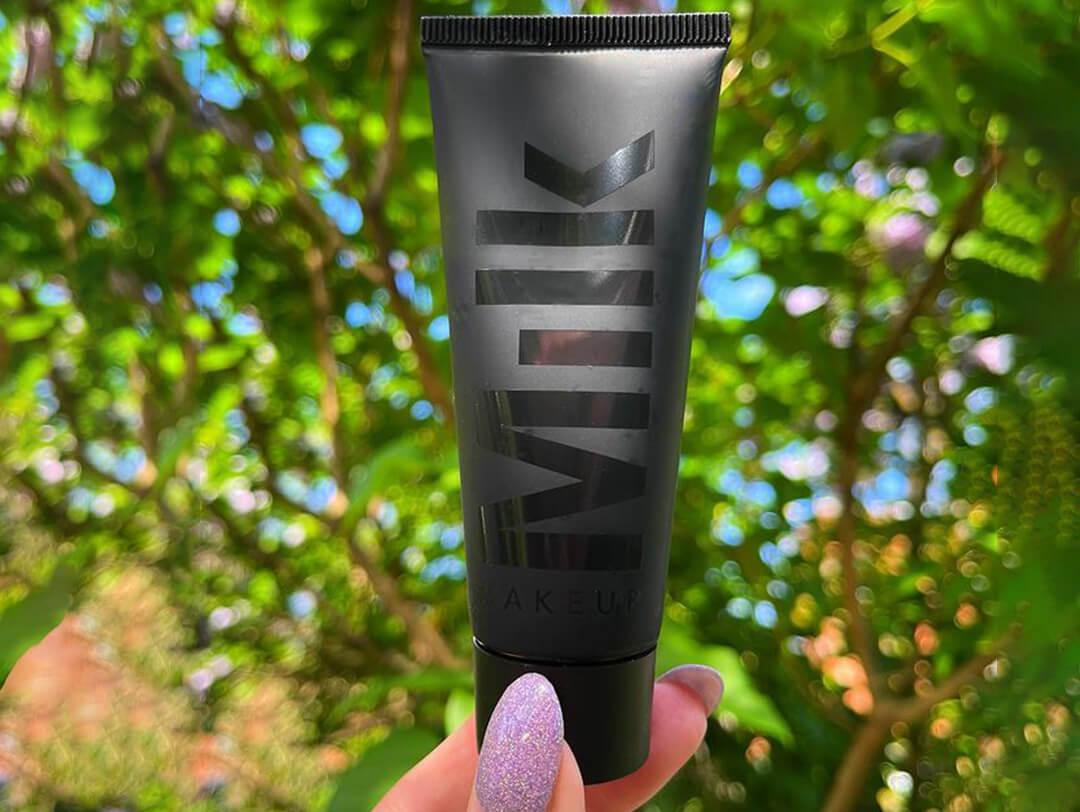 A close photo of a hand holding a MILK MAKEUP Pore Eclipse Mattifying + Blurring Makeup Primer with a tree background Desktop