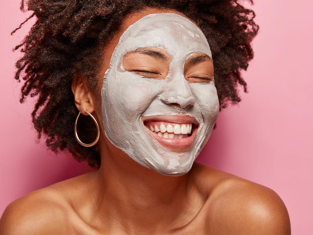 Close-up image of a smiling woman with mud mask on her face against pink background Desktop