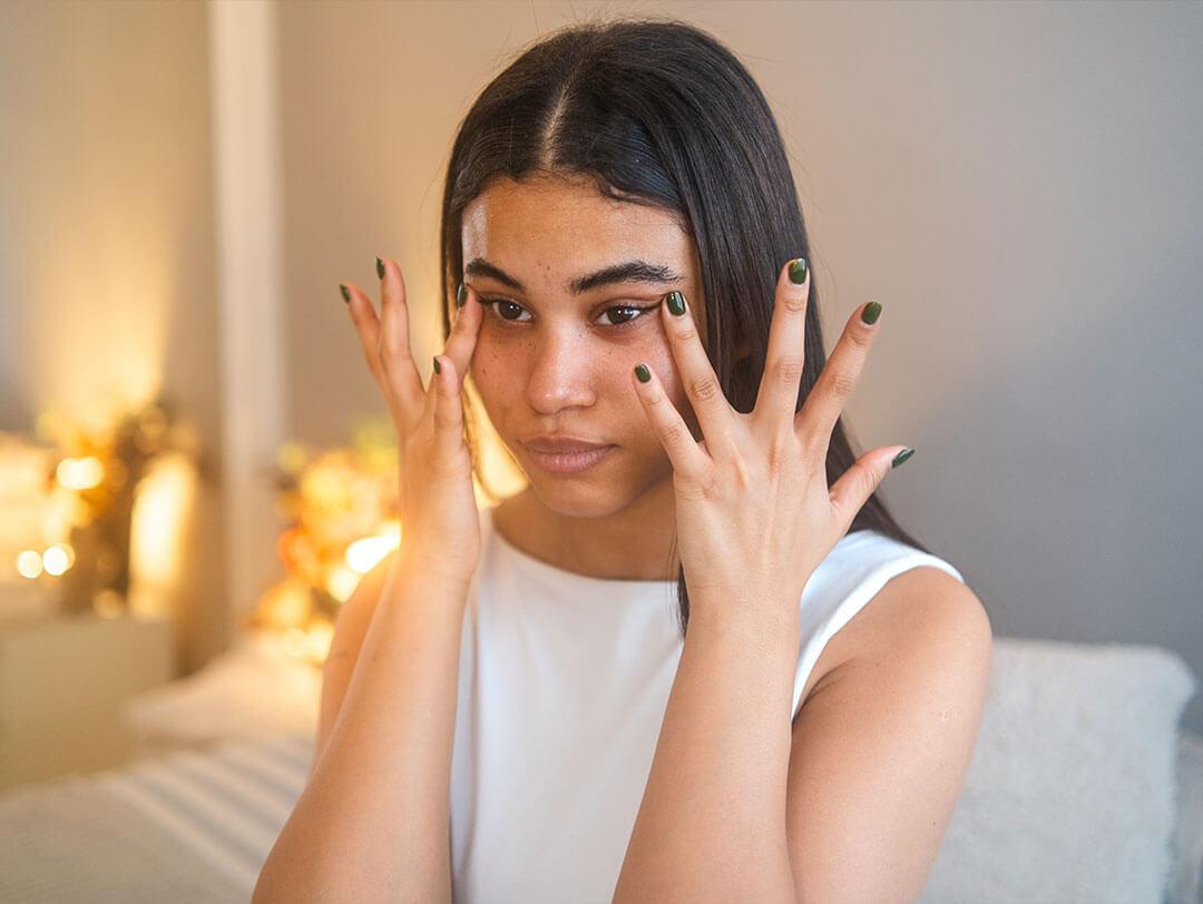 A young woman gently applying castor oil under her eyes with her fingers to treat dark circles Desktop