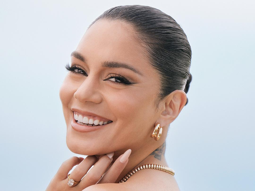 A beaming female celebrity adorned in gold earrings and a necklace, accompanied by a dazzling diamond ring captured in a close-up shot Desktop