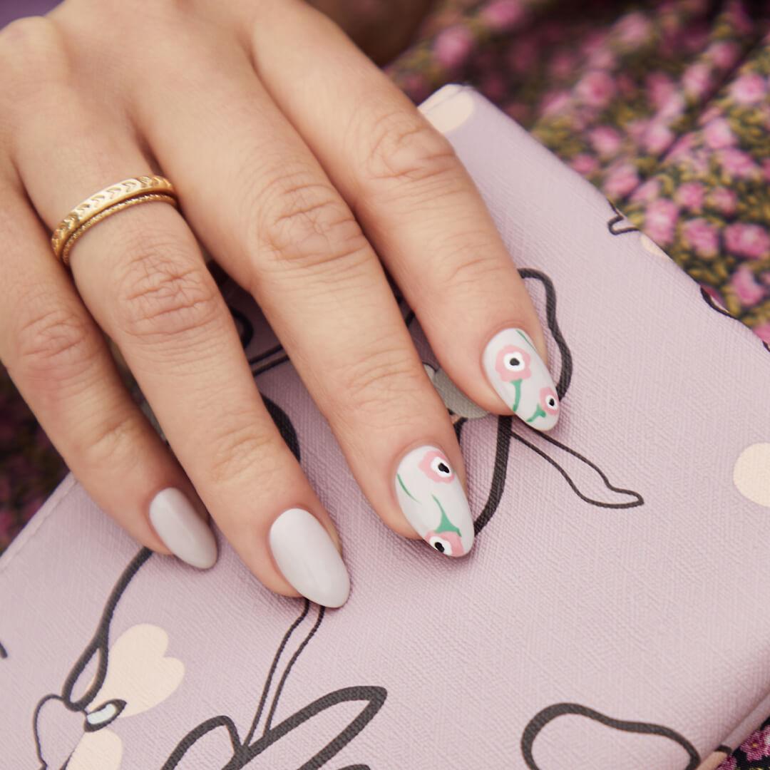 Close-up of a model's hand with light mint blue nail polish and pink floral accents holding the April 2020 IPSY Glam Bag Mobile