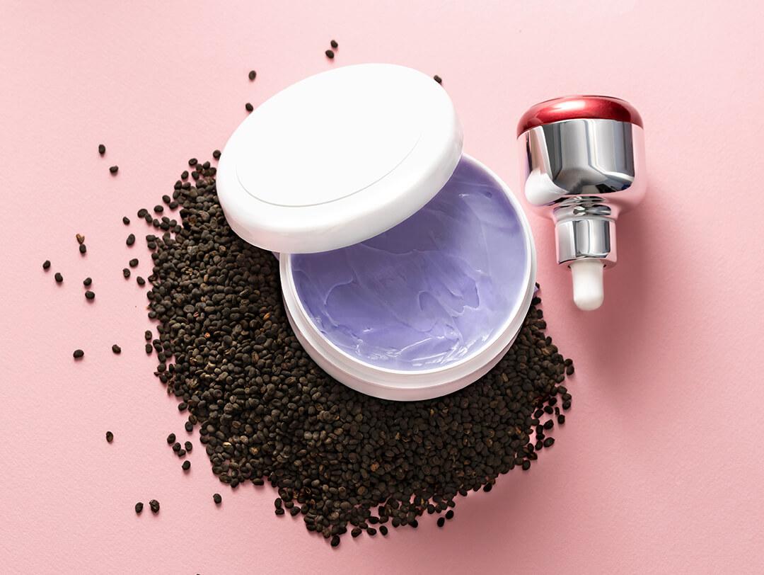 Babchi dry raw seeds (Psoralea Corylifolia) on pink surface with various kinds of cosmetic products Desktop