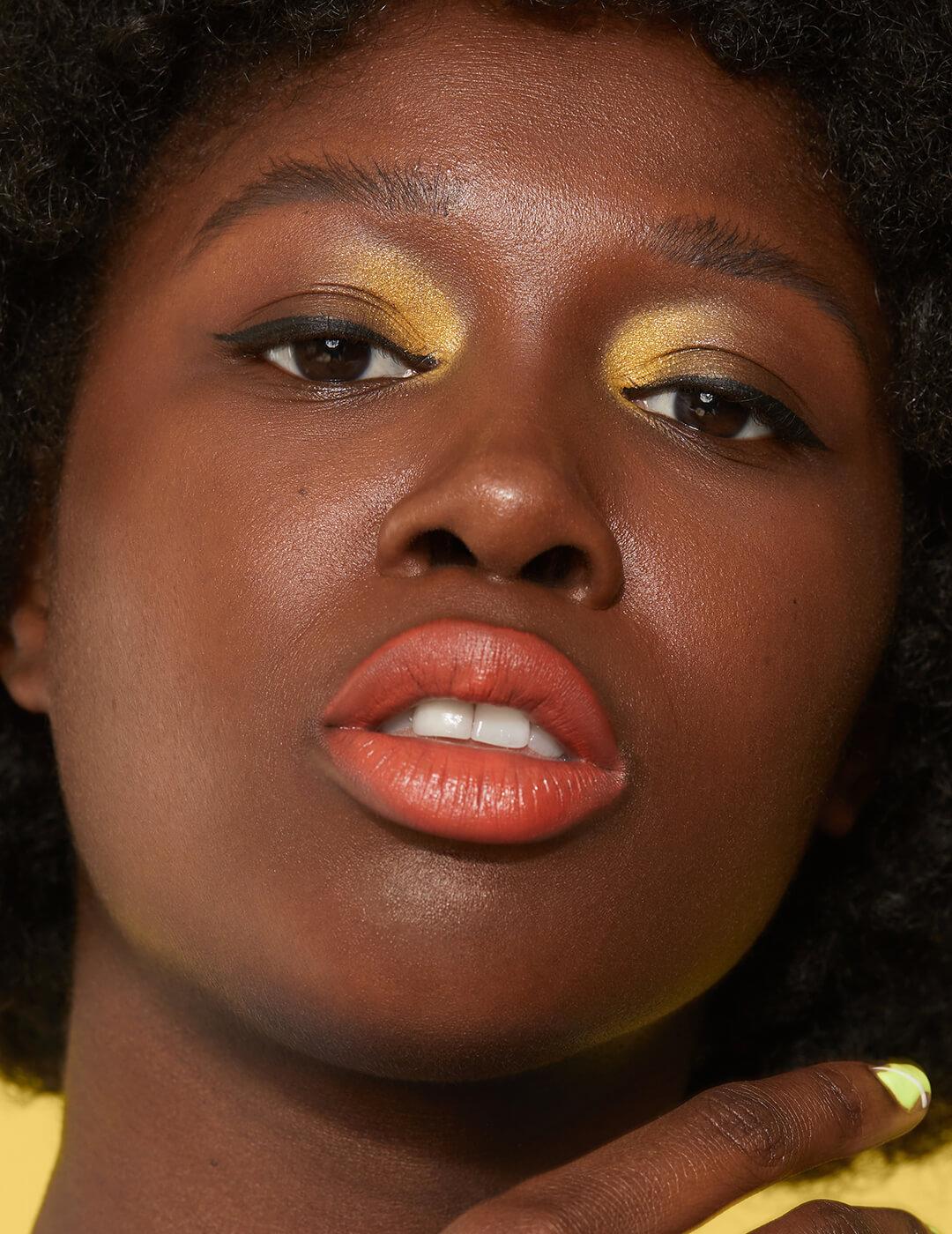 Close-up of a Black model rocking a gold inner corner eye makeup look and orange lips Desktop
