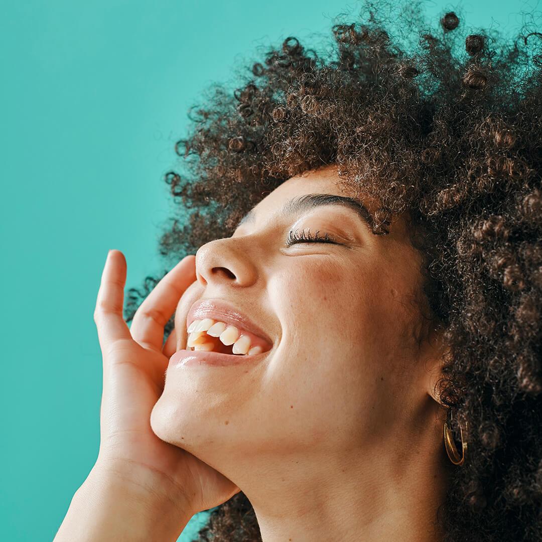 Photo of a model smiling on a teal background Mobile