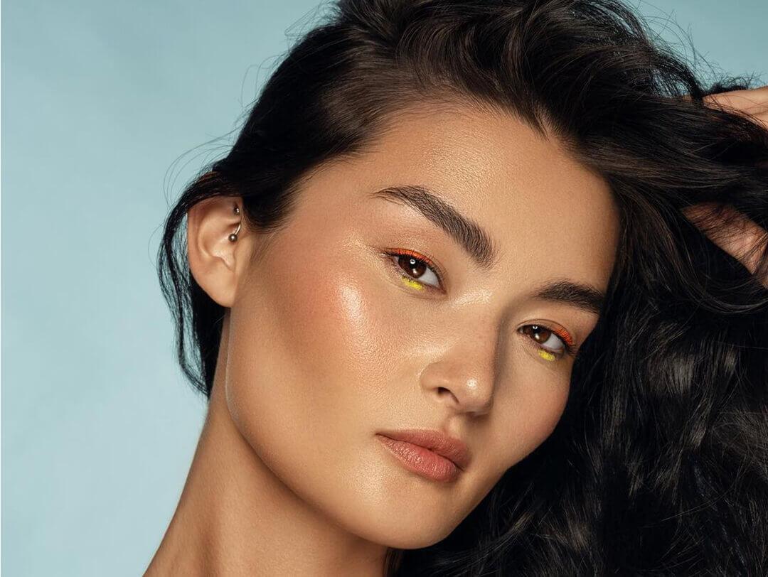 A photo of a woman showing her defined cheekbone and bright-colored eyeshadow on a pastel teal background Desktop