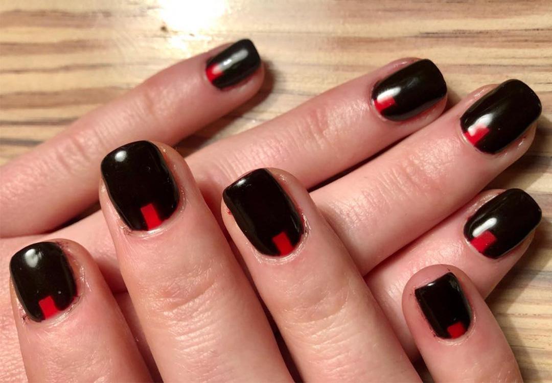 A closeup photo of a model's hand with a mix of red on black nail polish on a wooden background Desktop