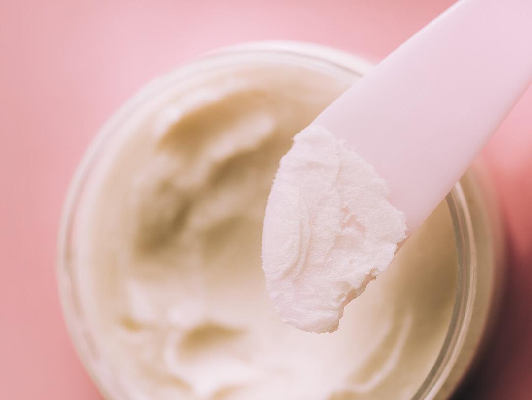 A jar of hardened coconut oil with pink spatula against pink background Mobile