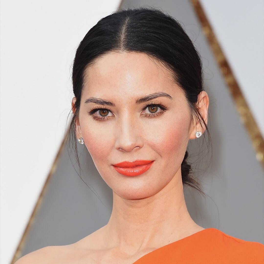 An image of Olivia Munn donning an orange off-the-shoulder dress, her black hair styled in a sleek low bun, and a fiery orange monochromatic makeup Desktop