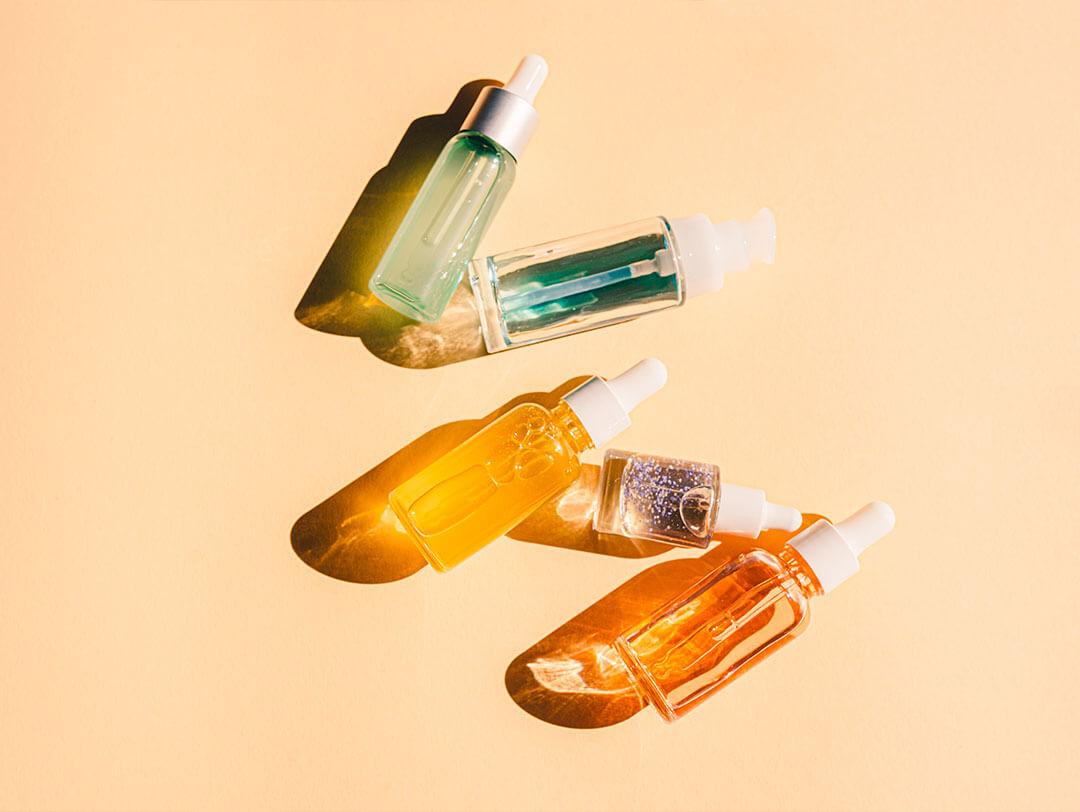 A flatlay of a variety of vibrant bottles containing liquids, serums, or gels on a peach-colored background Desktop