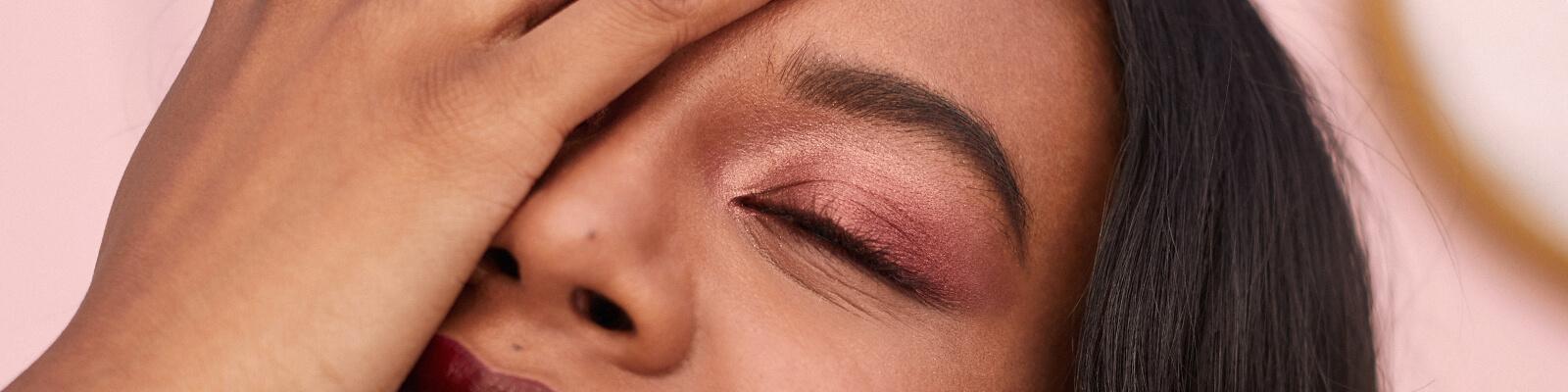 An image of a model rocking a rose gold eyeshadow look covering half of her face with her hand Desktop
