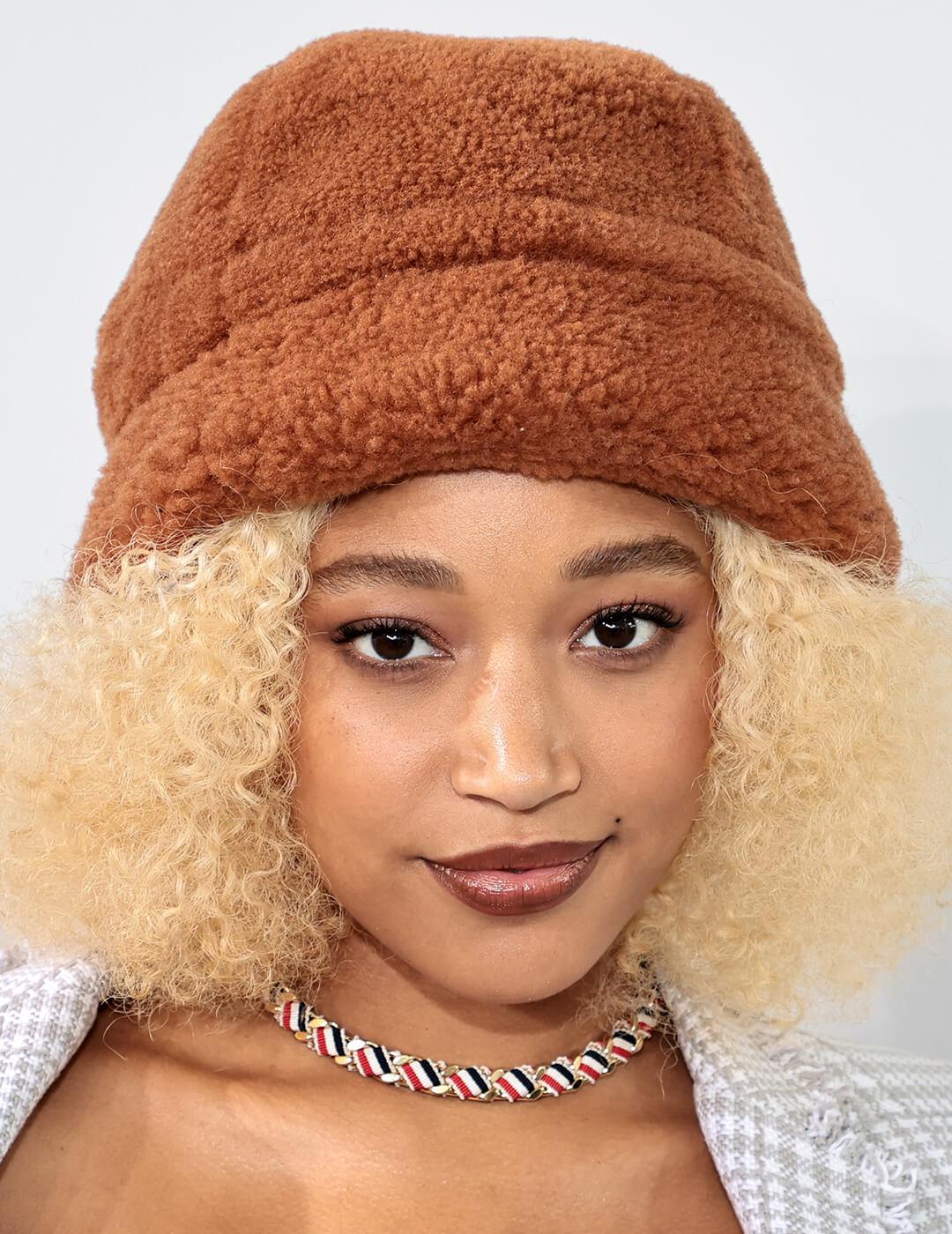 A photo of Amandla Stenberg with a brown hat and brown curly hair Mobile