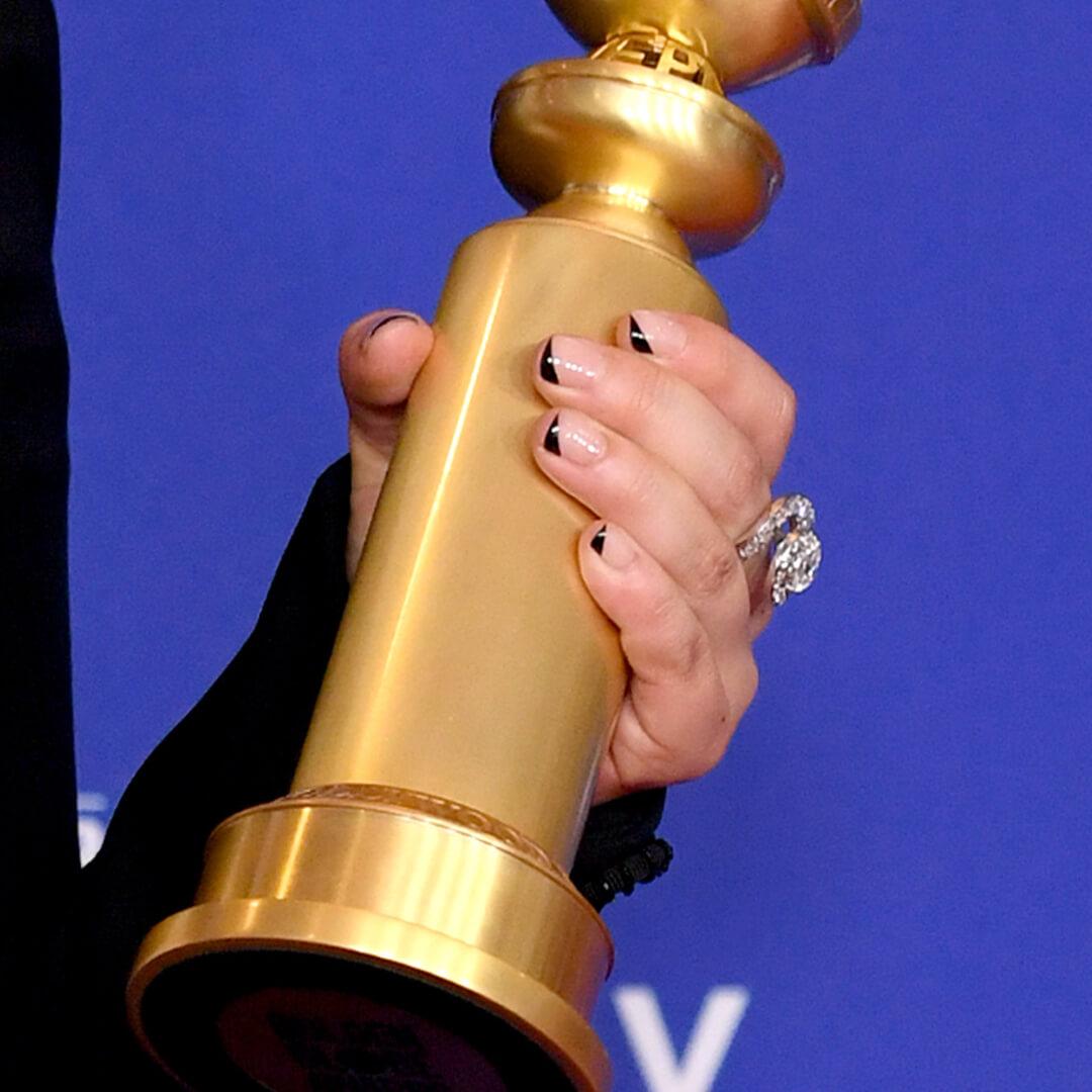 Close up of Awkwafina's hand with black French moon nail art holding a Golden Globes Award statuette Mobile