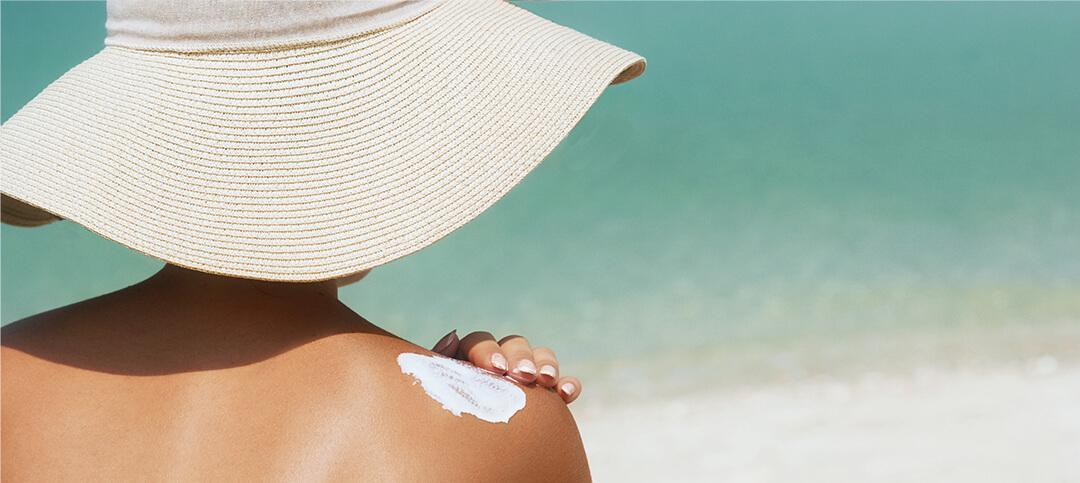 An image of a woman applying sunscreen on her shoulders. Desktop